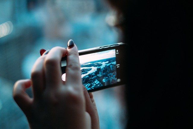 Detail rukou držících mobil, pořizujících fotografii
